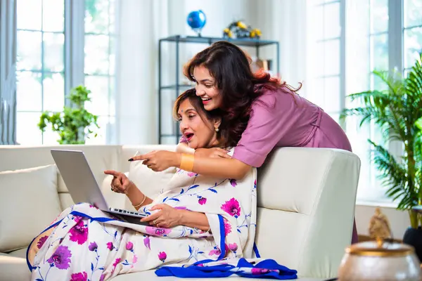 Yaşlı anne kız dizüstü bilgisayar kullanıyor, Hintli son sınıf öğrencisi sari giymiş genç kızı hem alışveriş yaparken, hem sörf yaparken, hem de modern evde kaliteli zaman geçirirken ekranda sarılıyor.