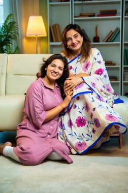 Yaşlı anne, kanepede otururken el ele tutuşarak sohbet ediyor. Hintli, Asyalı, sari giymiş yaşlı bir anne ve yanında oturan genç bir kız. Kapalı alanda samimi konuşmalar yapıyor.