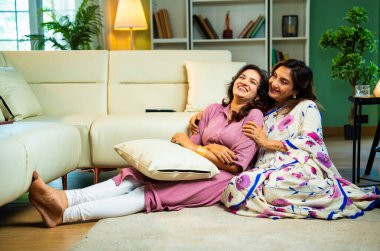 Yaşlı anne, kanepede otururken el ele tutuşarak sohbet ediyor. Hintli, Asyalı, sari giymiş yaşlı bir anne ve yanında oturan genç bir kız. Kapalı alanda samimi konuşmalar yapıyor.