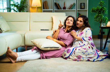 Yaşlı anne, kanepede otururken el ele tutuşarak sohbet ediyor. Hintli, Asyalı, sari giymiş yaşlı bir anne ve yanında oturan genç bir kız. Kapalı alanda samimi konuşmalar yapıyor.