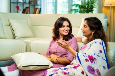 Yaşlı anne, kanepede otururken el ele tutuşarak sohbet ediyor. Hintli, Asyalı, sari giymiş yaşlı bir anne ve yanında oturan genç bir kız. Kapalı alanda samimi konuşmalar yapıyor.