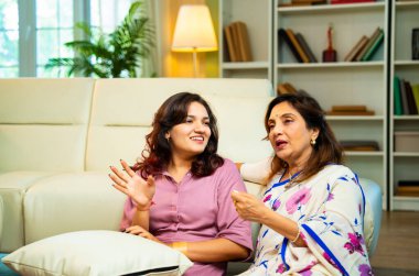 Yaşlı anne, kanepede otururken el ele tutuşarak sohbet ediyor. Hintli, Asyalı, sari giymiş yaşlı bir anne ve yanında oturan genç bir kız. Kapalı alanda samimi konuşmalar yapıyor.