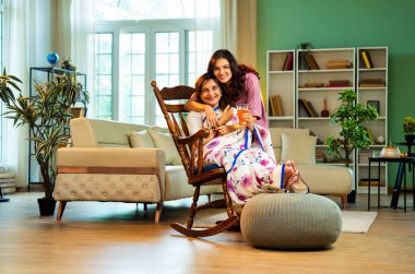 Kızı kıdemli anne suyu servis ediyor, sallanan sandalyede oturan Hintli Asyalı yaşlı kadın genç kızından bir bardak taze portakal suyu alıyor ve modern evde sohbet ediyor.