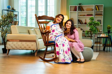 Kızı kıdemli anne suyu servis ediyor, sallanan sandalyede oturan Hintli Asyalı yaşlı kadın genç kızından bir bardak taze portakal suyu alıyor ve modern evde sohbet ediyor.