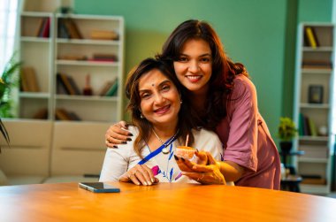 Annenin doğum gününü evde pastayla kutlayan Hintli kız, mumla aydınlatılmış kek ile yaşlı anneye sürpriz yapıyor. Hem gülümsüyor, hem mum üflüyor, sarılıyor, modern oturma odasında sevgisini gösteriyor.