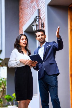 Hintli iş adamları dışarıda buluşuyor, resmi takım elbiseli Asyalı kadın ve erkek proje detaylarını tartışıyor tablet ve kahveyle modern verandada duruyor, takım çalışması ve işbirliği gösteriyor.