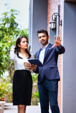 Hintli iş adamları dışarıda buluşuyor, resmi takım elbiseli Asyalı kadın ve erkek proje detaylarını tartışıyor tablet ve kahveyle modern verandada duruyor, takım çalışması ve işbirliği gösteriyor.