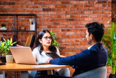 Hintli iş adamları dizüstü bilgisayar ve belge kullanıyorlar, Asyalı kurumsal erkek ve kadın resmi giyinmiş raporları tartışıyorlar, modern ofis masasında dizüstü bilgisayarla birlikte çalışıyorlar, takım çalışması kavramı.