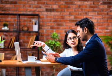 Hintli iş adamları dizüstü bilgisayar ve belge kullanıyorlar, Asyalı kurumsal erkek ve kadın resmi giyinmiş raporları tartışıyorlar, modern ofis masasında dizüstü bilgisayarla birlikte çalışıyorlar, takım çalışması kavramı.