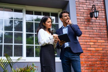 Hintli iş adamları dışarıda buluşuyor, resmi takım elbiseli Asyalı kadın ve erkek proje detaylarını tartışıyor tablet ve kahveyle modern verandada duruyor, takım çalışması ve işbirliği gösteriyor.