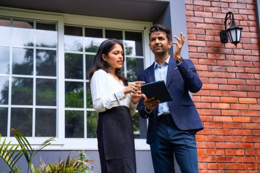 Hintli iş adamları dışarıda buluşuyor, resmi takım elbiseli Asyalı kadın ve erkek proje detaylarını tartışıyor tablet ve kahveyle modern verandada duruyor, takım çalışması ve işbirliği gösteriyor.