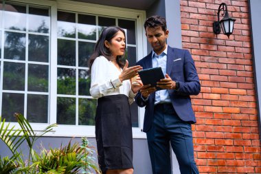 Hintli iş adamları dışarıda buluşuyor, resmi takım elbiseli Asyalı kadın ve erkek proje detaylarını tartışıyor tablet ve kahveyle modern verandada duruyor, takım çalışması ve işbirliği gösteriyor.