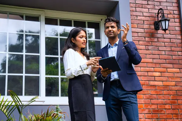 Hintli iş adamları dışarıda buluşuyor, resmi takım elbiseli Asyalı kadın ve erkek proje detaylarını tartışıyor tablet ve kahveyle modern verandada duruyor, takım çalışması ve işbirliği gösteriyor.