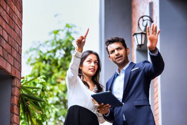 Hintli iş adamları dışarıda buluşuyor, resmi takım elbiseli Asyalı kadın ve erkek proje detaylarını tartışıyor tablet ve kahveyle modern verandada duruyor, takım çalışması ve işbirliği gösteriyor.
