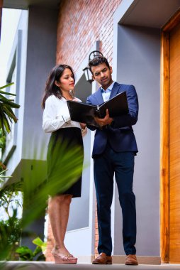 Hintli iş adamları dışarıda yürüyor, şirket adamı ve kadın modern ofis verandasında yürürken iş tartışıyorlar, dosya ve kahve tutuyorlar, takım çalışması ve profesyonel işbirliği sergiliyorlar.