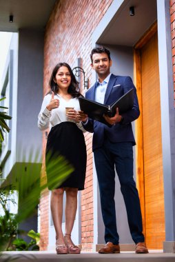 Hintli iş adamları dışarıda yürüyor, şirket adamı ve kadın modern ofis verandasında yürürken iş tartışıyorlar, dosya ve kahve tutuyorlar, takım çalışması ve profesyonel işbirliği sergiliyorlar.