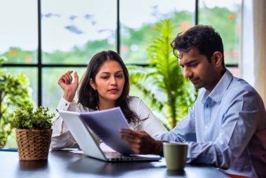 Hintli iş adamları dizüstü bilgisayar ve belge kullanıyorlar, Asyalı kurumsal erkek ve kadın resmi giyinmiş raporları tartışıyorlar, modern ofis masasında dizüstü bilgisayarla birlikte çalışıyorlar, takım çalışması kavramı.