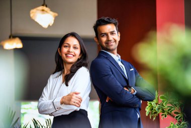 Hintli iş adamları başarıyı kutluyor, 30 'lu yaşlarda Asyalı kurumsal erkek kadın resmi profesyonel kıyafetler giyiyor, özgüvenle gülümsüyor ve modern ofiste kamera önünde birlikte poz veriyorlar.