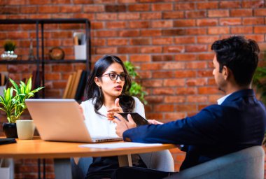 Hintli iş adamları dizüstü bilgisayar ve belge kullanıyorlar, Asyalı kurumsal erkek ve kadın resmi giyinmiş raporları tartışıyorlar, modern ofis masasında dizüstü bilgisayarla birlikte çalışıyorlar, takım çalışması kavramı.