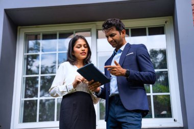 Hintli iş adamları dışarıda buluşuyor, resmi takım elbiseli Asyalı kadın ve erkek proje detaylarını tartışıyor tablet ve kahveyle modern verandada duruyor, takım çalışması ve işbirliği gösteriyor.