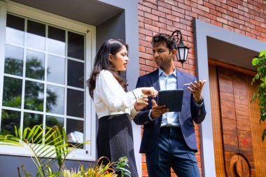 Hintli iş adamları dışarıda buluşuyor, resmi takım elbiseli Asyalı kadın ve erkek proje detaylarını tartışıyor tablet ve kahveyle modern verandada duruyor, takım çalışması ve işbirliği gösteriyor.