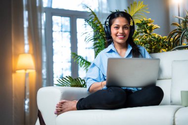 Başarılı Hintli iş kadını evinde ya da ofisinde dizüstü bilgisayar kullanarak online başarısını neşeli bir ifadeyle kutluyor ve kameraya güvenle bakarken yumruğunu kaldırıyor.