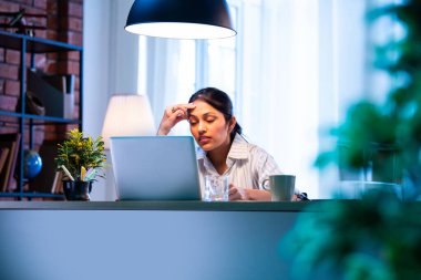 Hintli iş kadını, modern rahat ofiste dizüstü bilgisayar başında çalışırken baş ağrısı çekiyor, Asyalı genç bayan iş yükü ve fiziksel baskıyla uğraşırken stres ve boyun sertliği belirtileri gösteriyor.