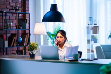 Modern rahat ofisteki belgelerle telefon görüşmesine katılan iş kadını. Ofis saatlerinde cep telefonuyla iletişim kuran Hintli Asyalı kadın. Güvenilir bir ifadeyle.
