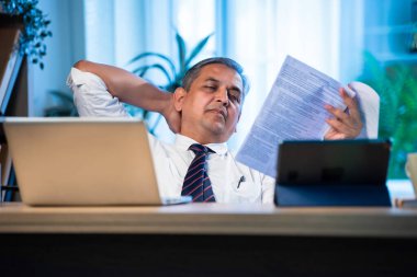 Hintli işadamı, şirket kaybını, stresi, gerilimi ve baskıyı temsil eden finansal belgeleri analiz eden Asyalı şirket yöneticisi, modern ofiste masa başında otururken raporları okumaktan endişe duyuyordu.