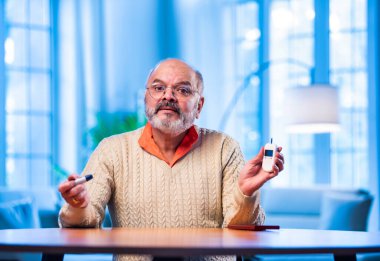 Hindistanlı kıdemli adam evde şeker seviyesini kontrol ediyor, el bilgisayarı kullanıyor, anormal okumalar gördükten sonra üzgün görünüyor, sağlık sorunlarını paylaşmak için akıllı telefondan birini arıyor.