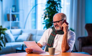 Hintli üst düzey bir adam, vergi raporlarını evde, masada CA ile görüşüyor. Gelir vergisi doldurma sezonunda muhasebeciye danışırken mutlu, yaşlı bir insan gülümsüyor.