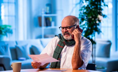 Hintli üst düzey bir adam, vergi raporlarını evde, masada CA ile görüşüyor. Gelir vergisi doldurma sezonunda muhasebeciye danışırken mutlu, yaşlı bir insan gülümsüyor.