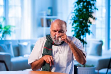 Hintli son sınıf öğrencisi modern evdeki masada otururken su içiyor. Kuru boğazdan kurtulan olgun Asyalı erkek, evde susuz ve sağlıklı bir şekilde yaşlanıyor.