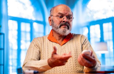 Hindistanlı kıdemli adam evde şeker seviyesini kontrol ediyor, el bilgisayarı kullanıyor, anormal okumalar gördükten sonra üzgün görünüyor, sağlık sorunlarını paylaşmak için akıllı telefondan birini arıyor.