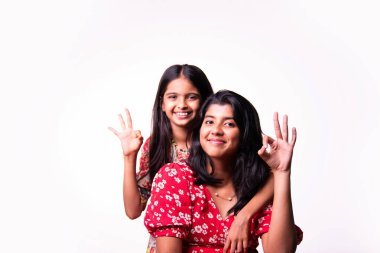 Beyaz arka planda dururken kameraya sarılıp gülümseyen Hintli küçük kardeş kızlar. Renkli elbiseler içinde Asyalı küçük kız kardeşler neşeli ifadelerle sevgi ve neşe gösteriyorlar.
