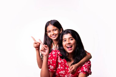 Beyaz arka planda dururken kameraya sarılıp gülümseyen Hintli küçük kardeş kızlar. Renkli elbiseler içinde Asyalı küçük kız kardeşler neşeli ifadelerle sevgi ve neşe gösteriyorlar.