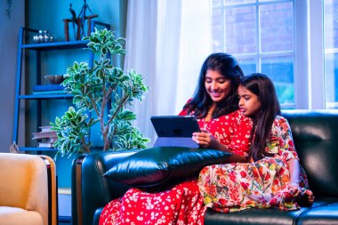 Hintli küçük kız kardeşler tablet bilgisayarda komik videolar izlerken evde oturuyorlar, Asyalı kız kardeşler dijital eğlencenin, çocukluk eğlencesinin, mutluluğun, aile bağlarının tadını çıkarıyorlar.