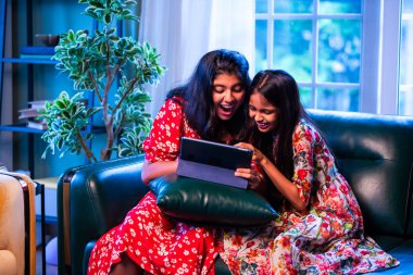 Hintli küçük kız kardeşler tablet bilgisayarda komik videolar izlerken evde oturuyorlar, Asyalı kız kardeşler dijital eğlencenin, çocukluk eğlencesinin, mutluluğun, aile bağlarının tadını çıkarıyorlar.