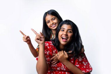 Hintli küçük kız kardeşler beyaz arka plana karşı boş alanı işaret ediyor, Asyalı küçük kardeşler fotokopi alanında el kol geziyor, neşeli ifadeler ve eğlenceli iletişim konsepti gösteren izole edilmiş stüdyo görüntüleri.