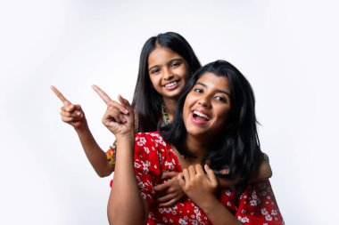 Hintli küçük kız kardeşler beyaz arka plana karşı boş alanı işaret ediyor, Asyalı küçük kardeşler fotokopi alanında el kol geziyor, neşeli ifadeler ve eğlenceli iletişim konsepti gösteren izole edilmiş stüdyo görüntüleri.