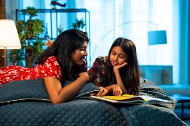 Hintli kardeş kardeşler kitap okurken birlikte sessiz zaman geçirmenin tadını çıkarıyorlar. Renkli kıyafetler giyen Asyalı küçük kızlar boş zamanlarında kapalı bir odada kitap okumaya odaklanırlar.