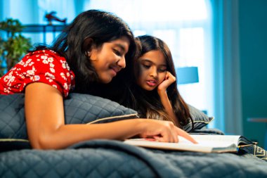 Hintli kardeş kardeşler kitap okurken birlikte sessiz zaman geçirmenin tadını çıkarıyorlar. Renkli kıyafetler giyen Asyalı küçük kızlar boş zamanlarında kapalı bir odada kitap okumaya odaklanırlar.