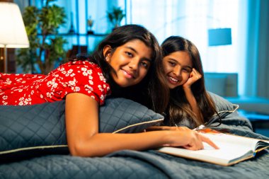 Hintli kardeş kardeşler kitap okurken birlikte sessiz zaman geçirmenin tadını çıkarıyorlar. Renkli kıyafetler giyen Asyalı küçük kızlar boş zamanlarında kapalı bir odada kitap okumaya odaklanırlar.