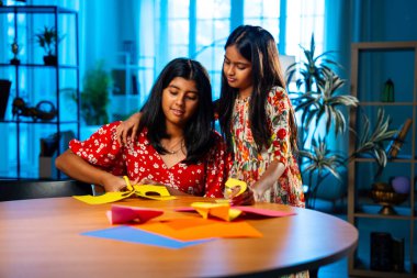 Hintli kardeş kardeşler içeride birlikte otururken makas kullanarak kağıt işi yapıyorlar. Küçük Asyalı kızlar rahat ev ortamında eğlenceli DIY etkinliği sırasında odak yaratıcılığıyla renkli çarşaf kesiyorlar.