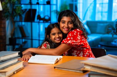 Hintli abla çalışma masasında evde otururken kalemle küçük kız kardeşine ders veriyor. Asyalı küçük kızlar ev ortamında ev ödevi yaparken birlikte öğrenme ve çalışma üzerine odaklandılar.