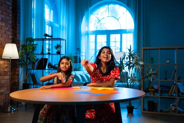 Hintli kardeş kardeşler içeride birlikte otururken makas kullanarak kağıt işi yapıyorlar. Küçük Asyalı kızlar rahat ev ortamında eğlenceli DIY etkinliği sırasında odak yaratıcılığıyla renkli çarşaf kesiyorlar.