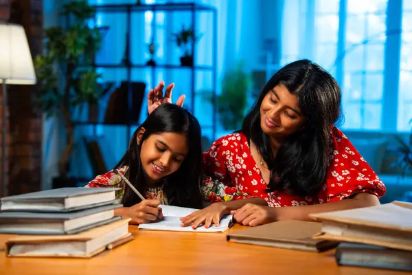 Hintli abla çalışma masasında evde otururken kalemle küçük kız kardeşine ders veriyor. Asyalı küçük kızlar ev ortamında ev ödevi yaparken birlikte öğrenme ve çalışma üzerine odaklandılar.