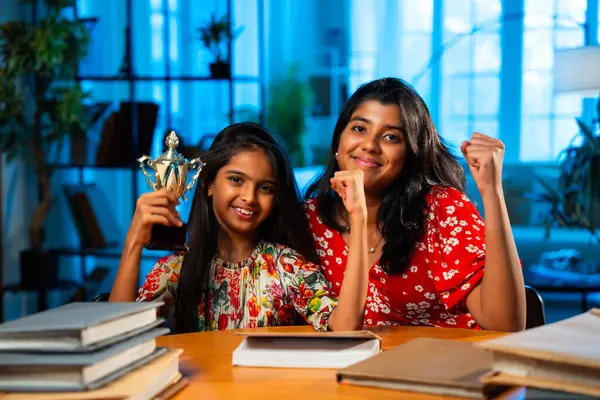 Küçük Hintli kız kitap ve kalemle otururken çalışma masasında ablasıyla caka satıyor. Asyalı küçük kardeşler gülümseyerek evde öğrenme ortamında başarıyı kutluyorlar.