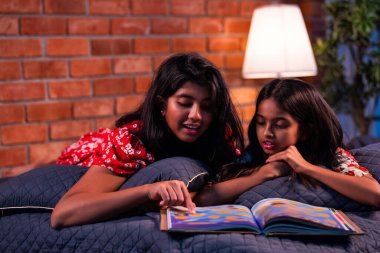 Hintli kardeş kardeşler kitap okurken birlikte sessiz zaman geçirmenin tadını çıkarıyorlar. Renkli kıyafetler giyen Asyalı küçük kızlar boş zamanlarında kapalı bir odada kitap okumaya odaklanırlar.