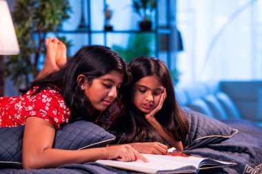 Hintli kardeş kardeşler kitap okurken birlikte sessiz zaman geçirmenin tadını çıkarıyorlar. Renkli kıyafetler giyen Asyalı küçük kızlar boş zamanlarında kapalı bir odada kitap okumaya odaklanırlar.